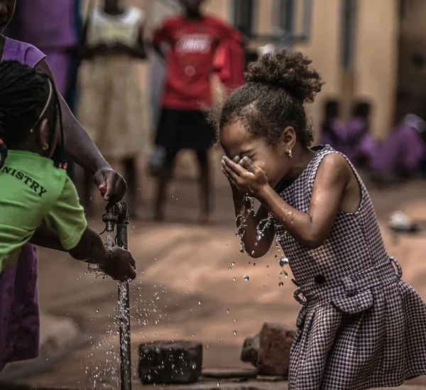 A young girl splashing her face with clean water from an outdoor tap